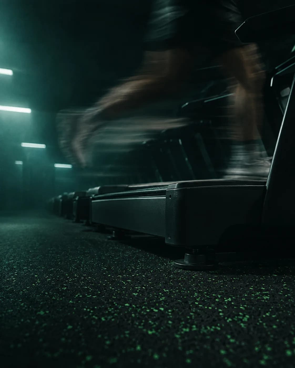 Une rangée de tapis de course sur un sol sombre, lumière rasante.