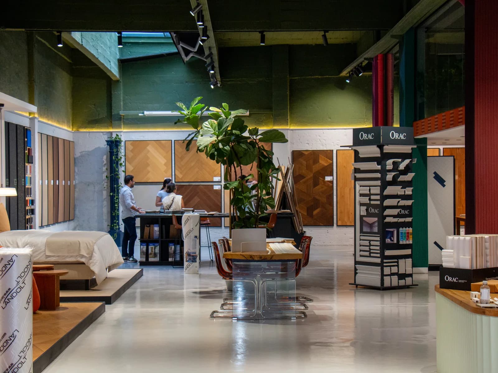 Le hall d’un showroom du groupe Worqbox : parquets exposés au mur, mobilier, une grande plante et le présentoir Orac.