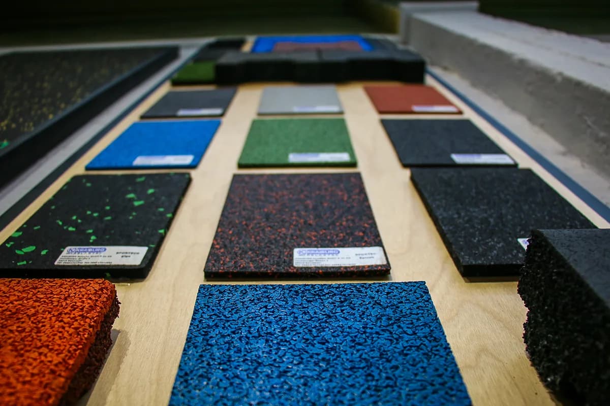 Des échantillons de sols SPORTEC en caoutchouc, unis ou mouchetés, alignés sur une table du showroom.